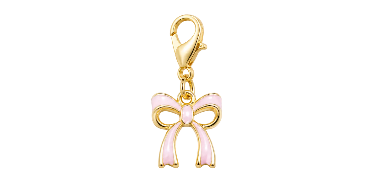 A gold charm shaped like a bow with light pink enamel details, attached to a gold lobster clasp, shown on a plain white background.